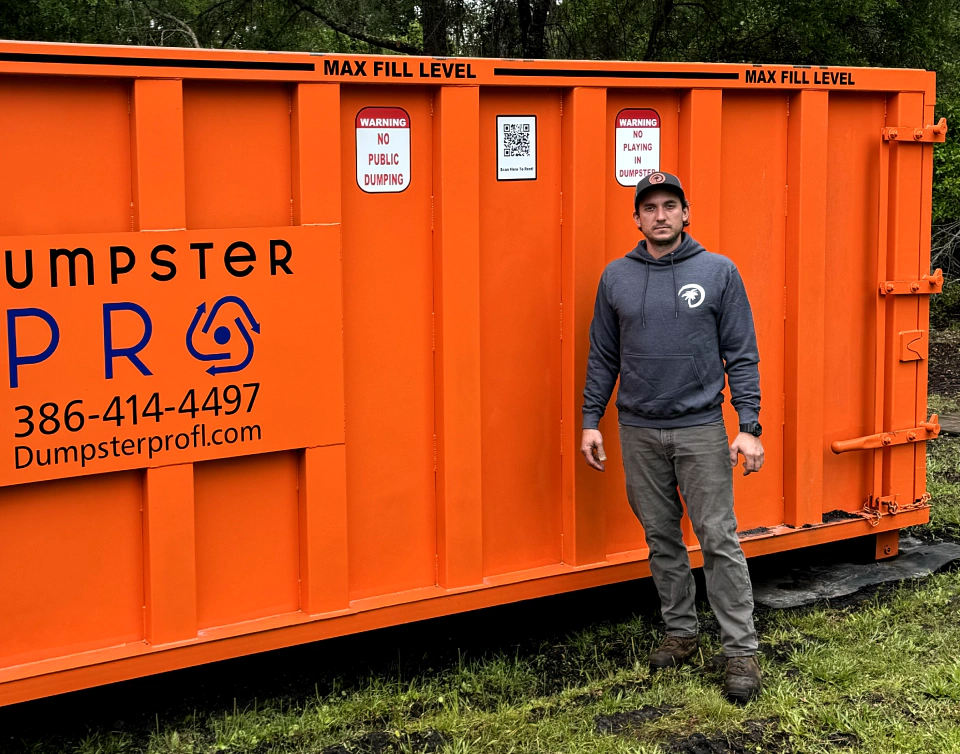 worker in the middle of a forest with an orange dumpster